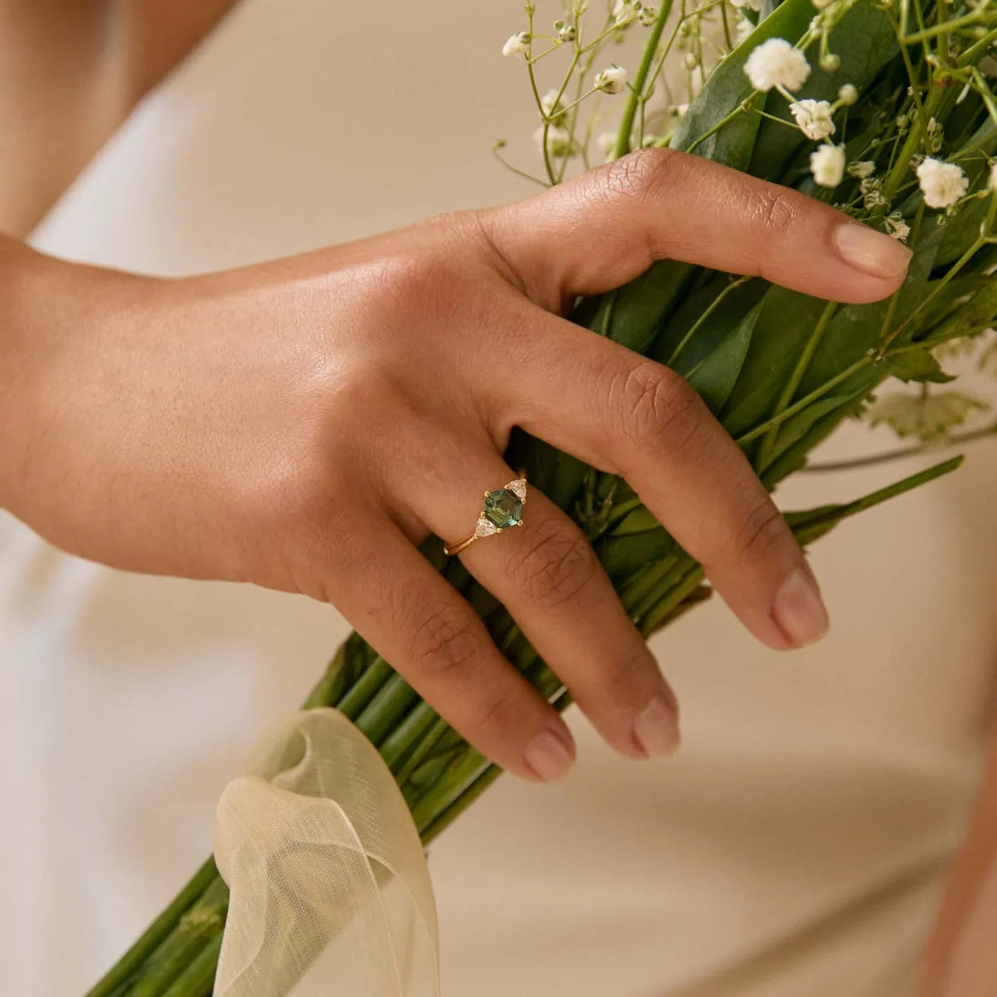 Person holding a bouquet of flowers with a focus on the hands wearing a hexagon sapphire engagement ring holding a bouquet.