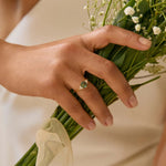 Person holding a bouquet of flowers with a focus on the hands wearing a hexagon sapphire engagement ring holding a bouquet.