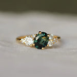 Gold ring with a green gemstone and smaller diamonds on a soft fabric background