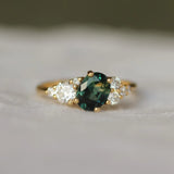 Gold ring with a green gemstone and smaller diamonds on a soft fabric background