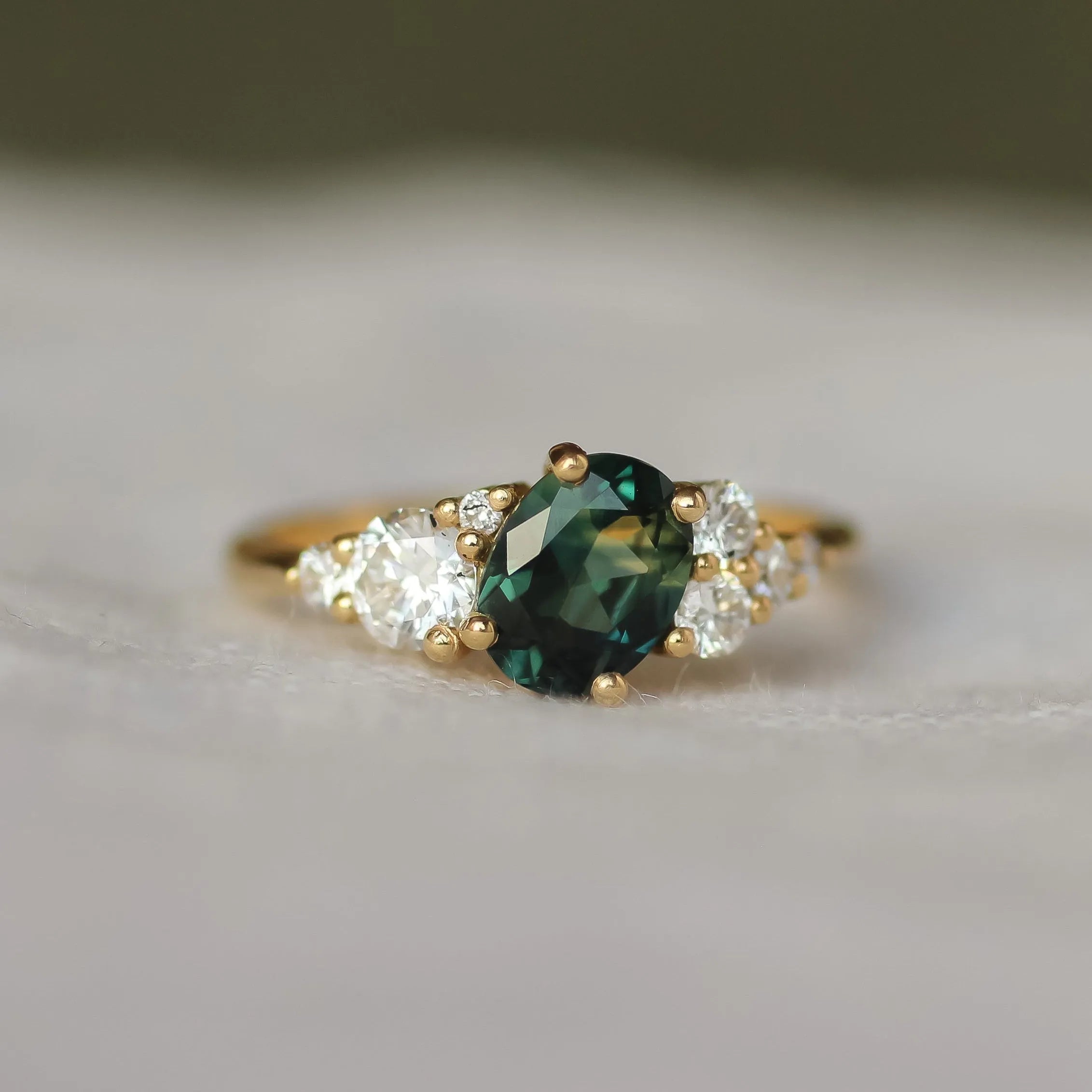 Gold ring with a green gemstone and smaller diamonds on a soft fabric background