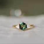 Gold ring with a green hexagon gemstone on a white fabric background