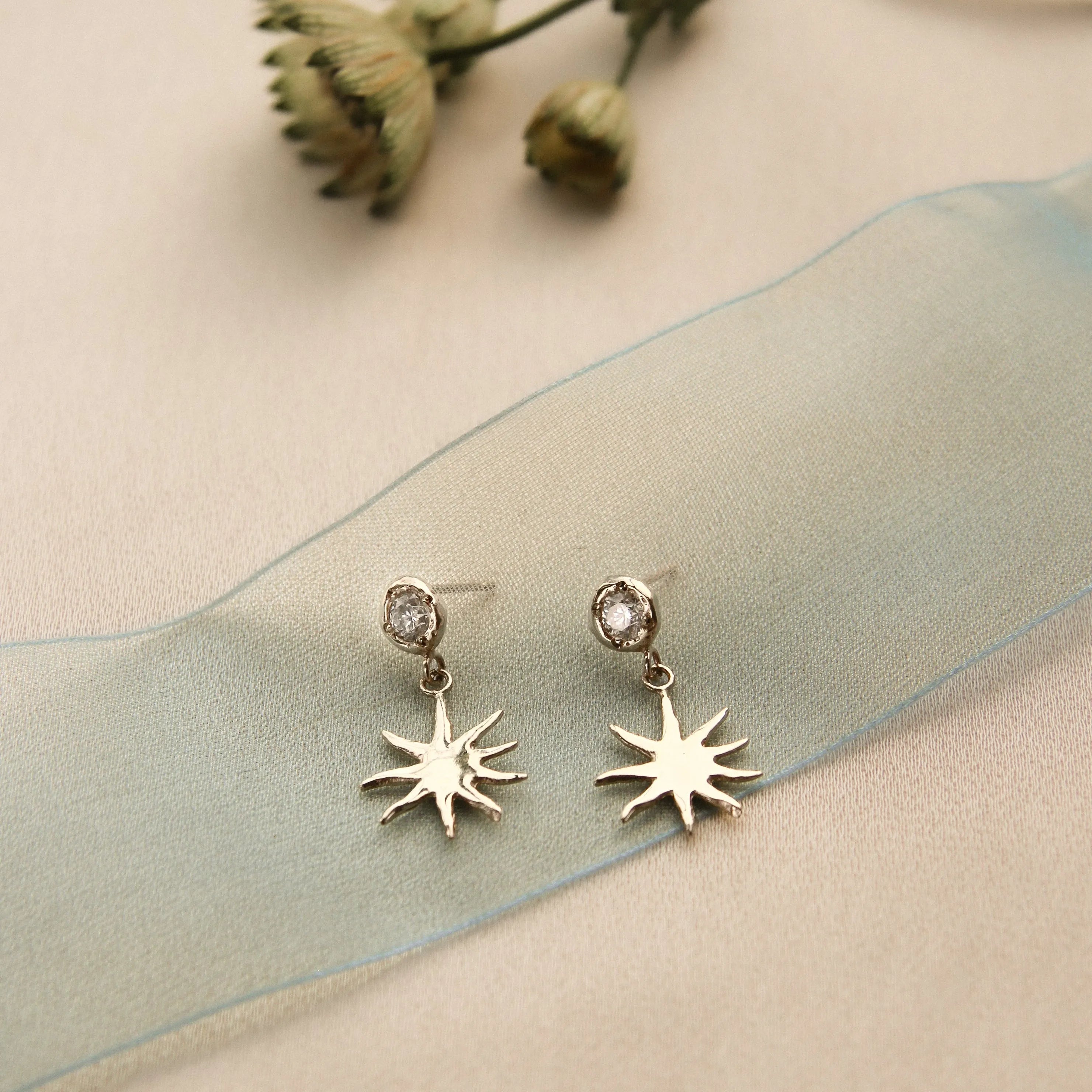 Sun-shaped earrings with a diamond stud detail on a soft fabric background