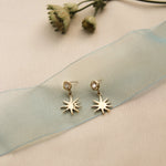 Gold star-shaped earrings on a soft fabric background with dried flowers.