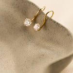 Gold earrings with round diamonds hooked onto the edge of a beige ceramic dish