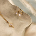 Gold open star necklace and hook earrings with round diamonds on a beige ceramic surface