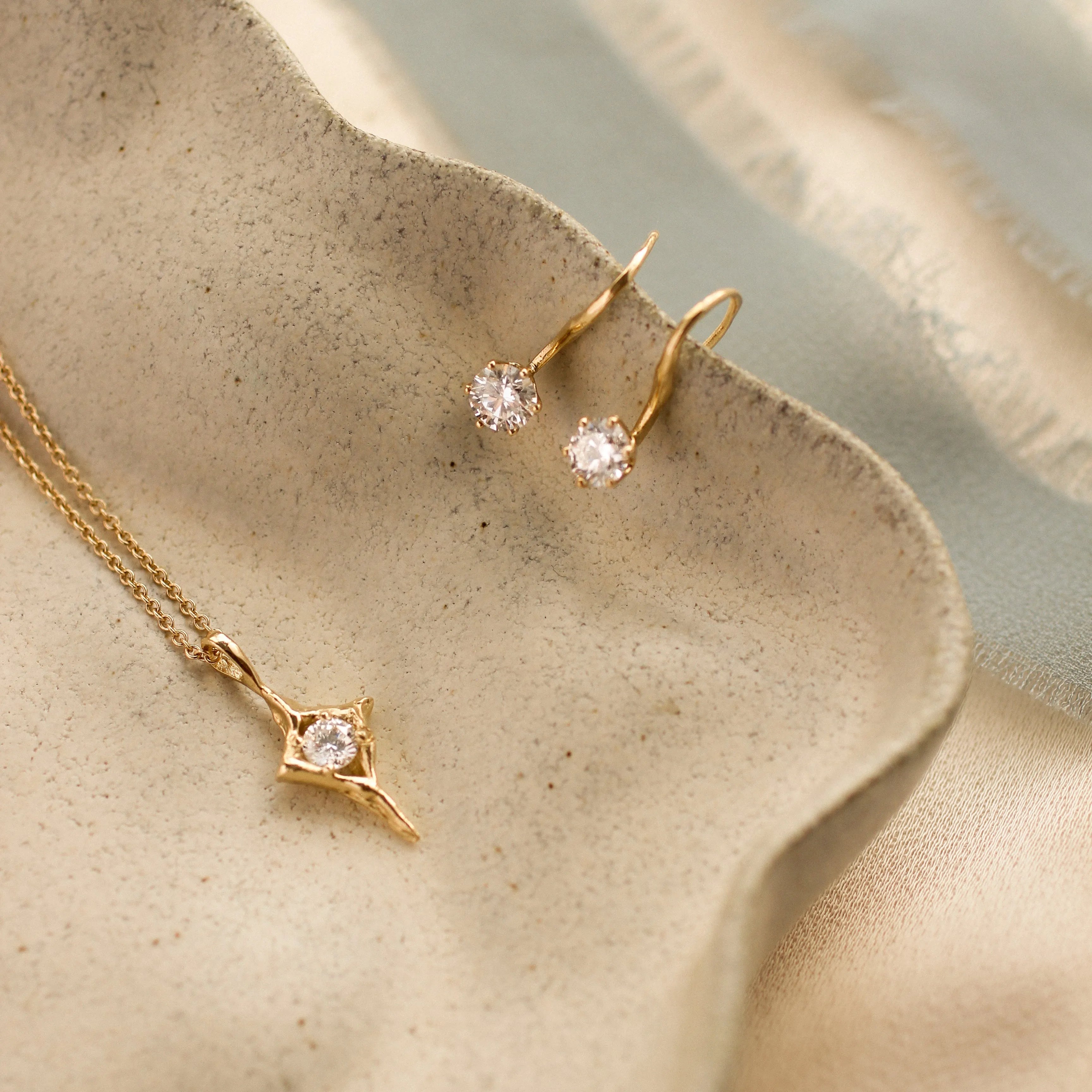 Gold open star necklace and hook earrings with round diamonds on a beige ceramic surface