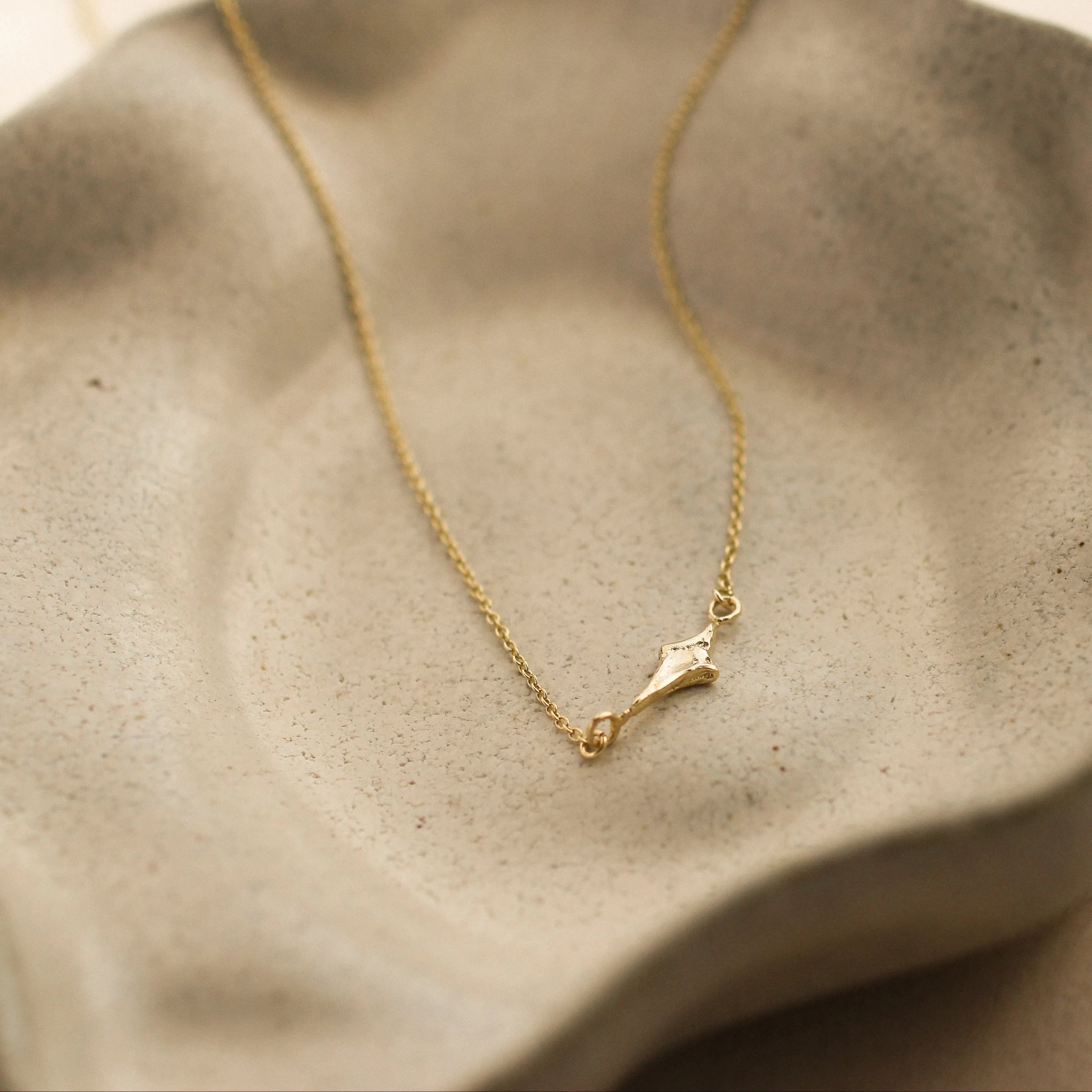 Gold necklace with four-pointed star charm on a textured beige ceramic dish