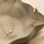 Gold necklace and earrings in four-point star shapes on a textured beige ceramic surface