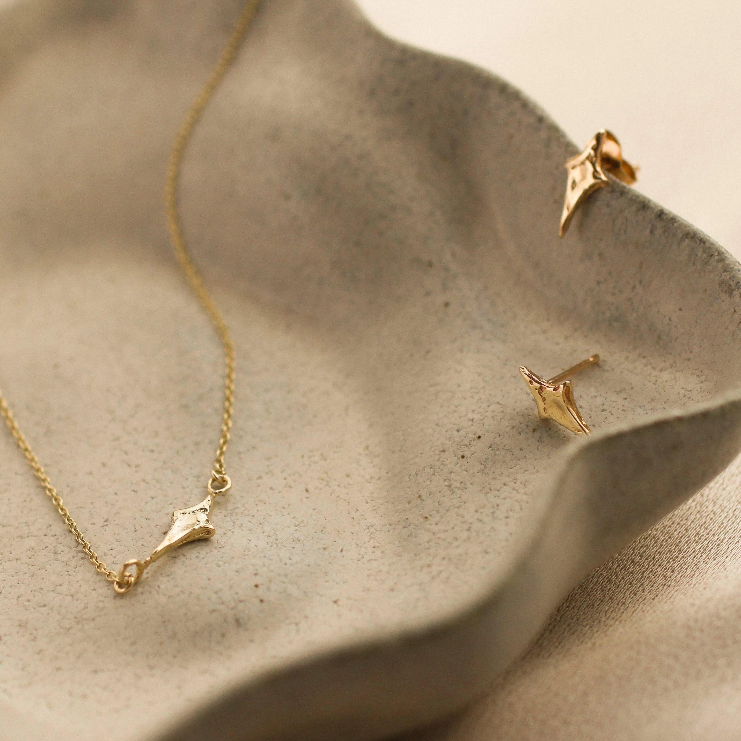 Gold necklace and earrings in four-point star shapes on a textured beige ceramic surface