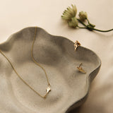Gold star-shaped necklace and earrings on a textured ceramic dish with a dried flower in the background.