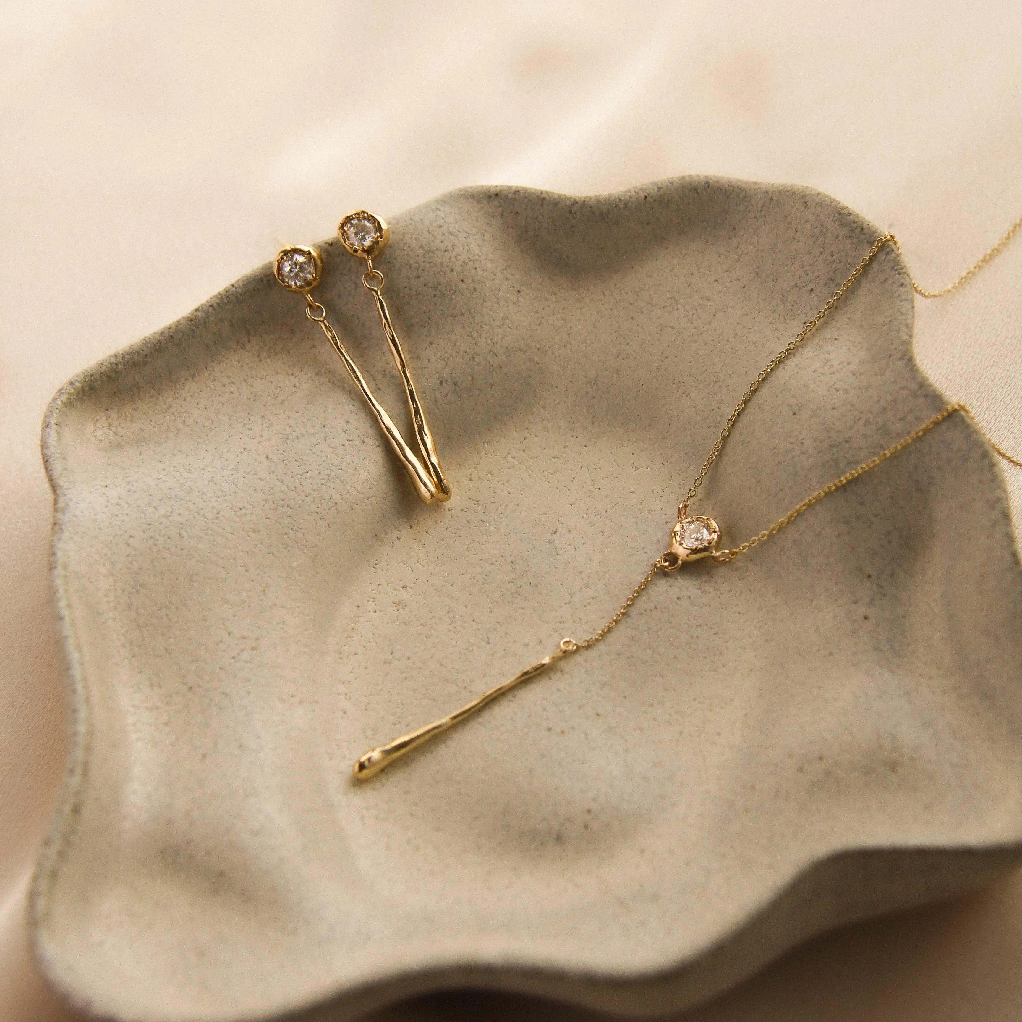 Gold necklace and earrings with diamond and molten texture on a textured stone surface