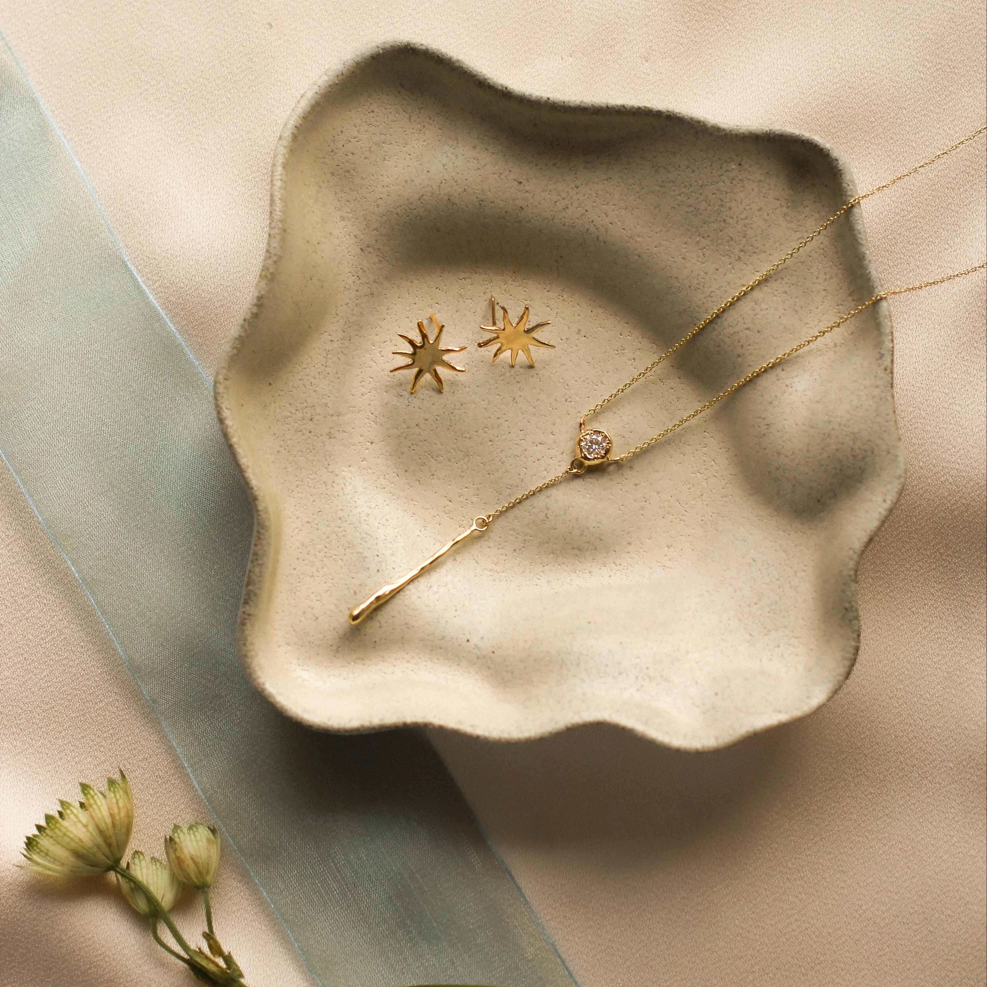 ceramic dish with diamond necklace and sun shaped stud earrings with flower and ribbon
