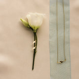flatlay of a white flower with star shaped earrings, and a matching necklace on a blue ribbon on a warm beige fabric