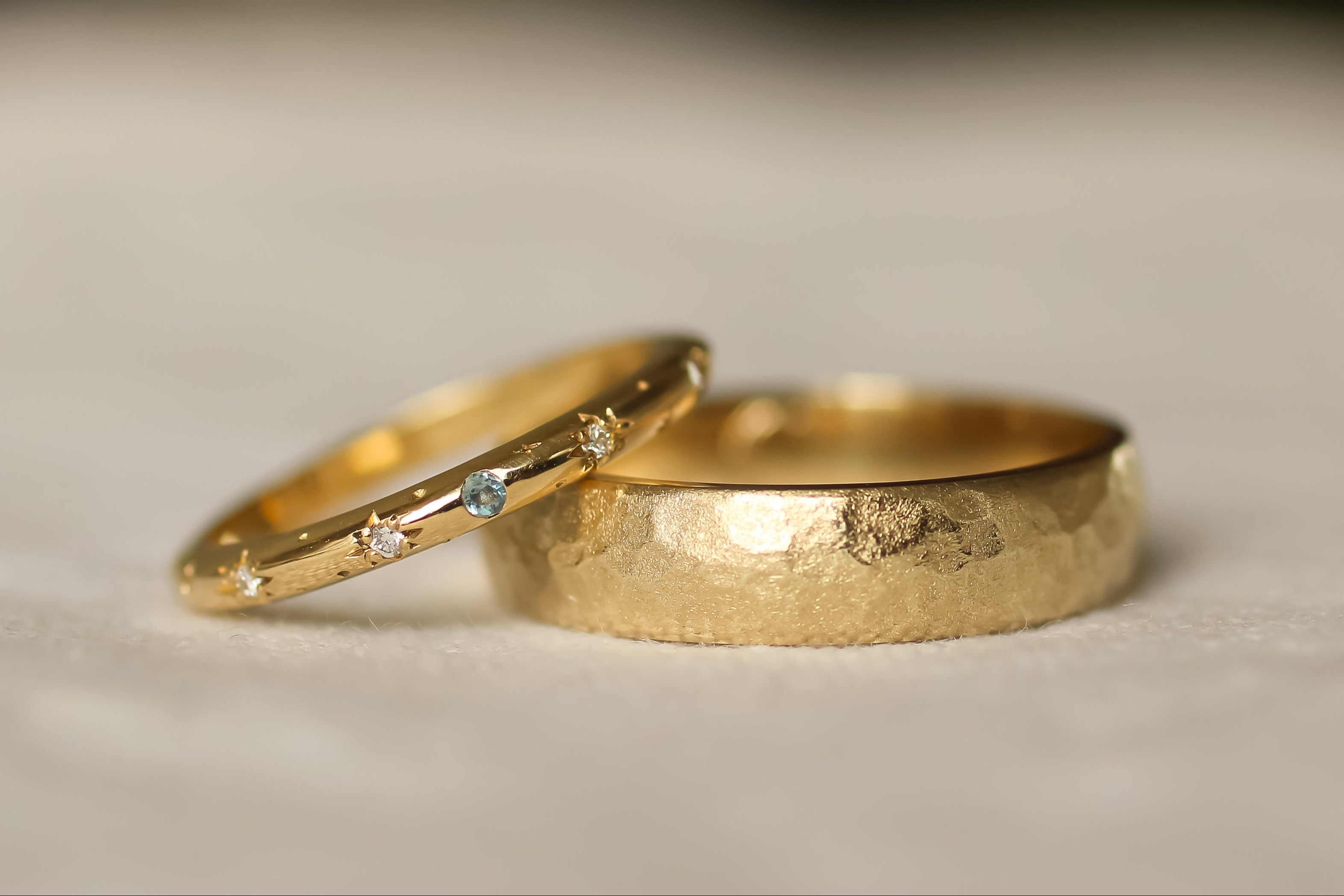 bespoke wedding rings with added aquamarine gemstone and layered textures with a blurred background 