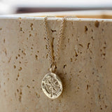 silver compass necklace with a pendant on a textured beige surface