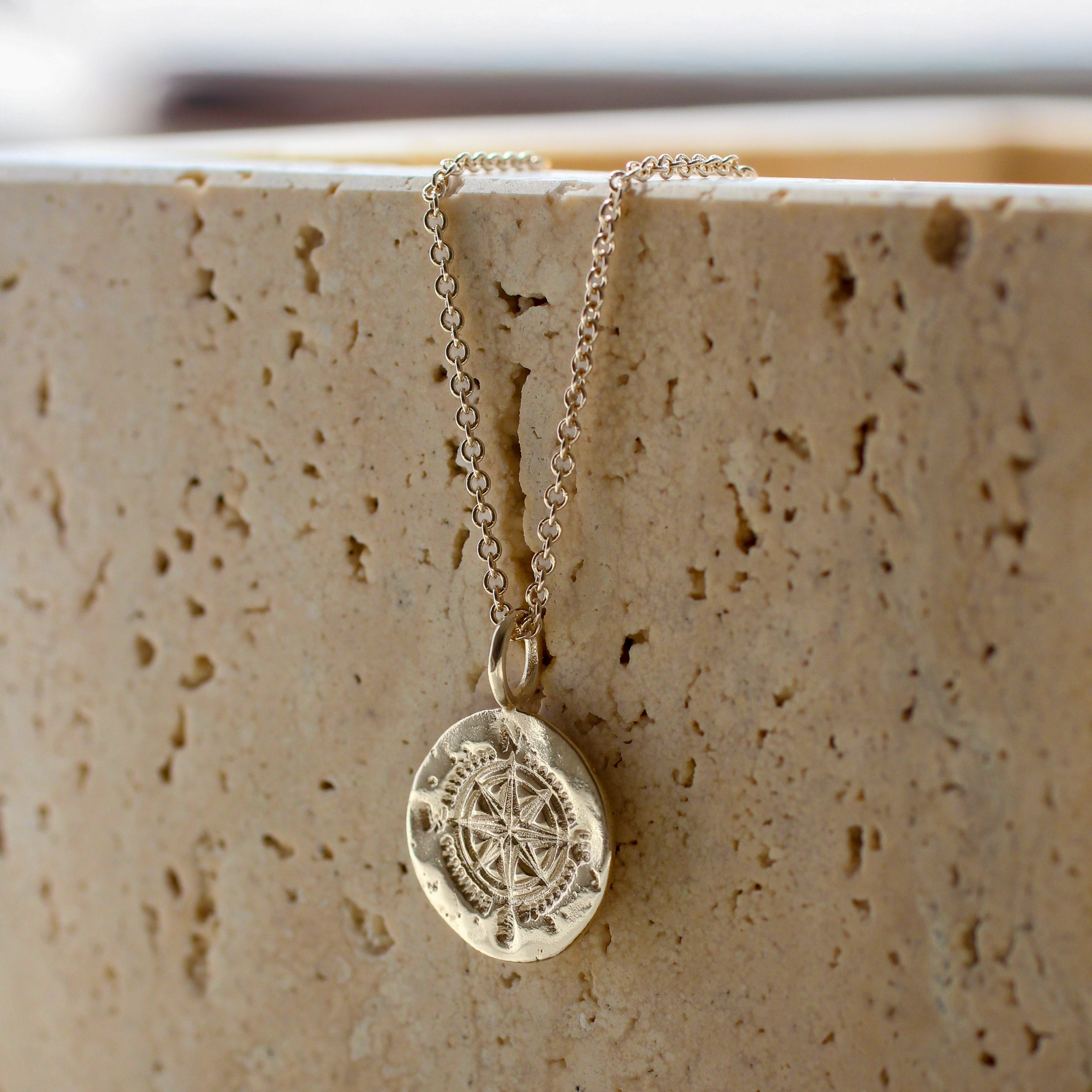 silver compass necklace with a pendant on a textured beige surface
