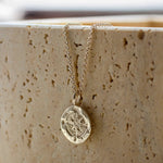 silver compass necklace with a pendant on a textured beige surface