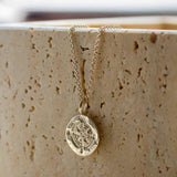 silver compass necklace with a pendant on a textured beige surface