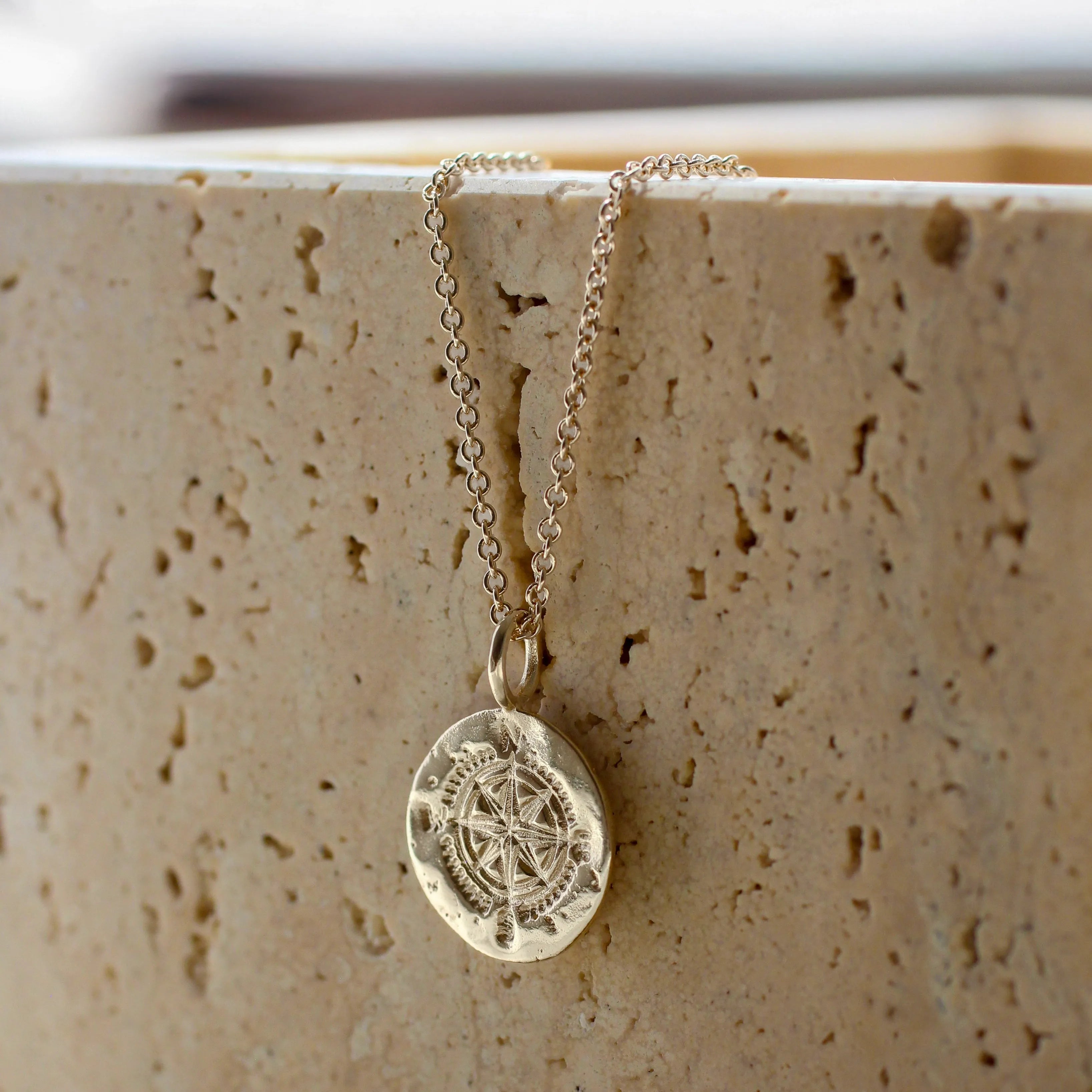 silver compass necklace with a pendant on a textured beige surface