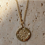 Gold necklace with a round compass pendant on a textured beige surface