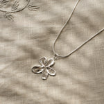 Silver flower pendant necklace on a textured beige fabric background