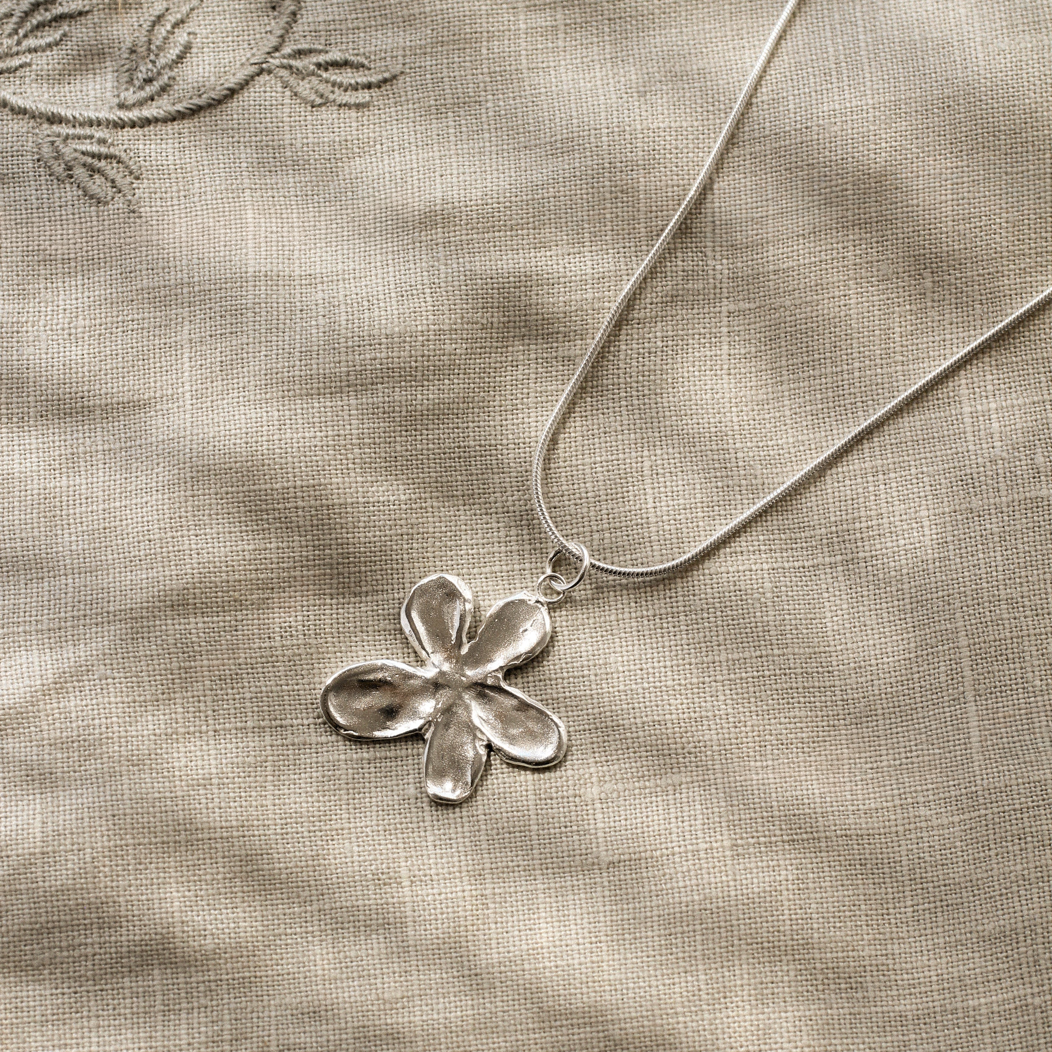 Silver flower pendant necklace on a textured beige fabric background