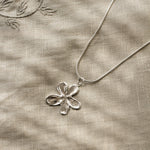 Silver flower pendant necklace on a textured beige fabric background