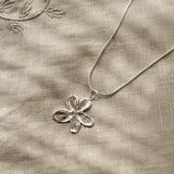 Silver flower pendant necklace on a textured beige fabric background