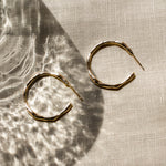 Gold hoop earrings on a textured beige fabric surface