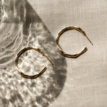 Gold hoop earrings on a textured beige fabric surface