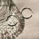 Pair of silver hoop earrings on a textured beige fabric surface