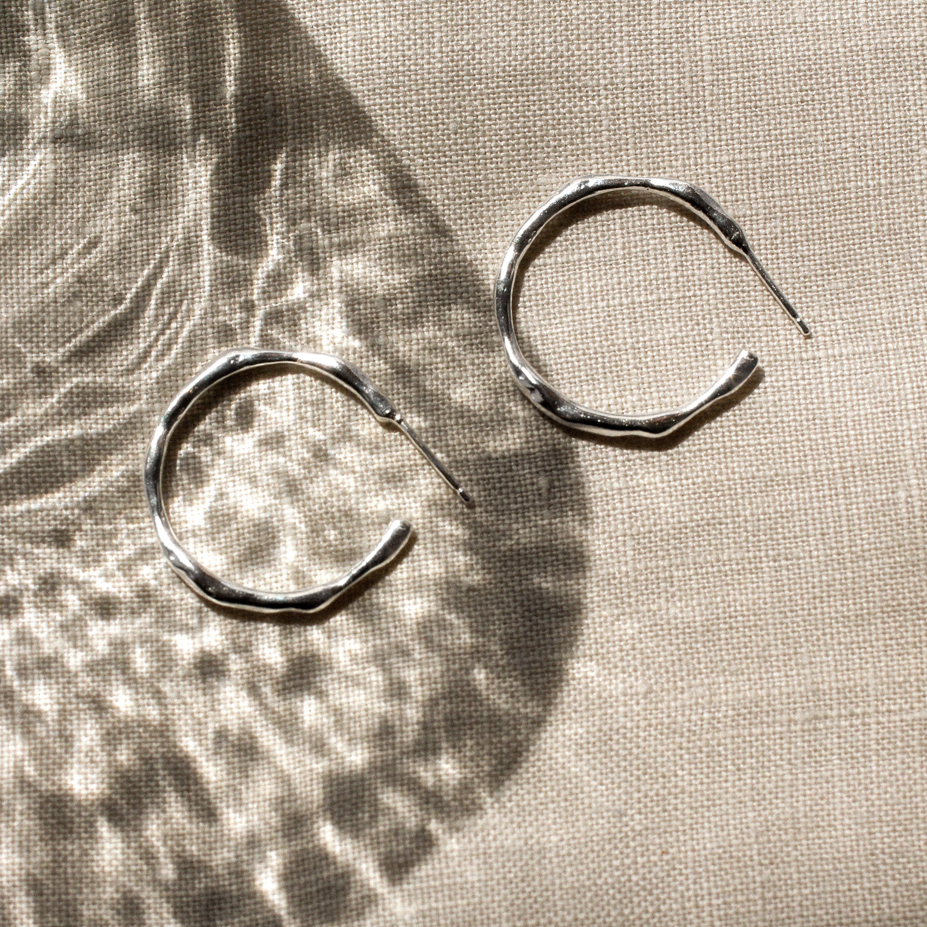 Pair of silver hoop earrings on a textured beige fabric surface