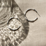 Pair of silver hoop earrings on a textured beige fabric surface