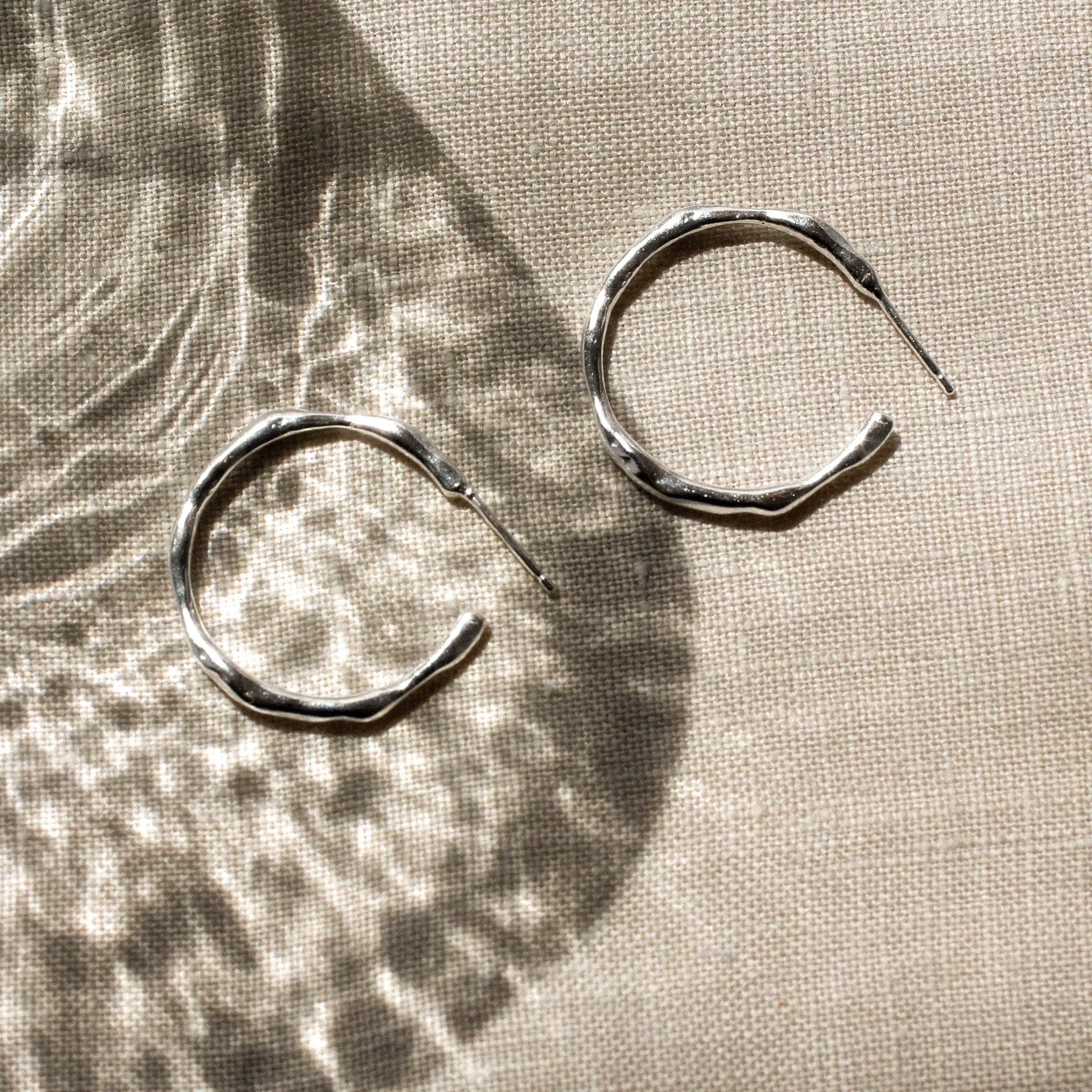 Pair of silver hoop earrings on a textured beige fabric surface