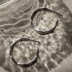 Pair of silver hoop earrings on a textured fabric surface
