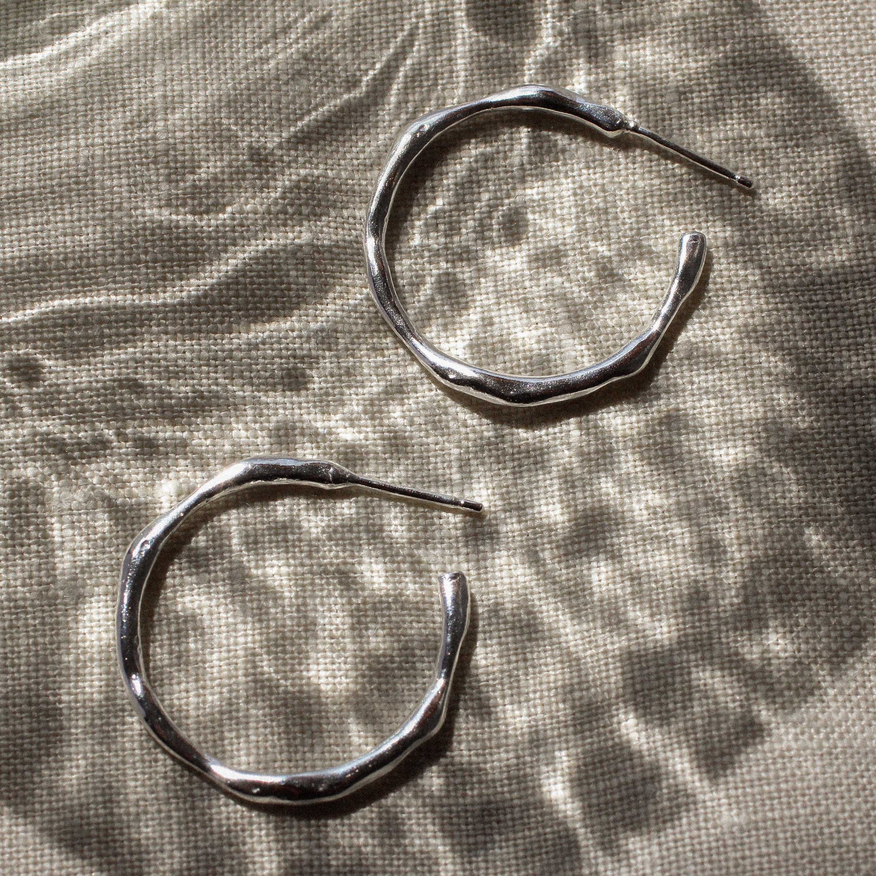 Pair of silver hoop earrings on a textured fabric surface
