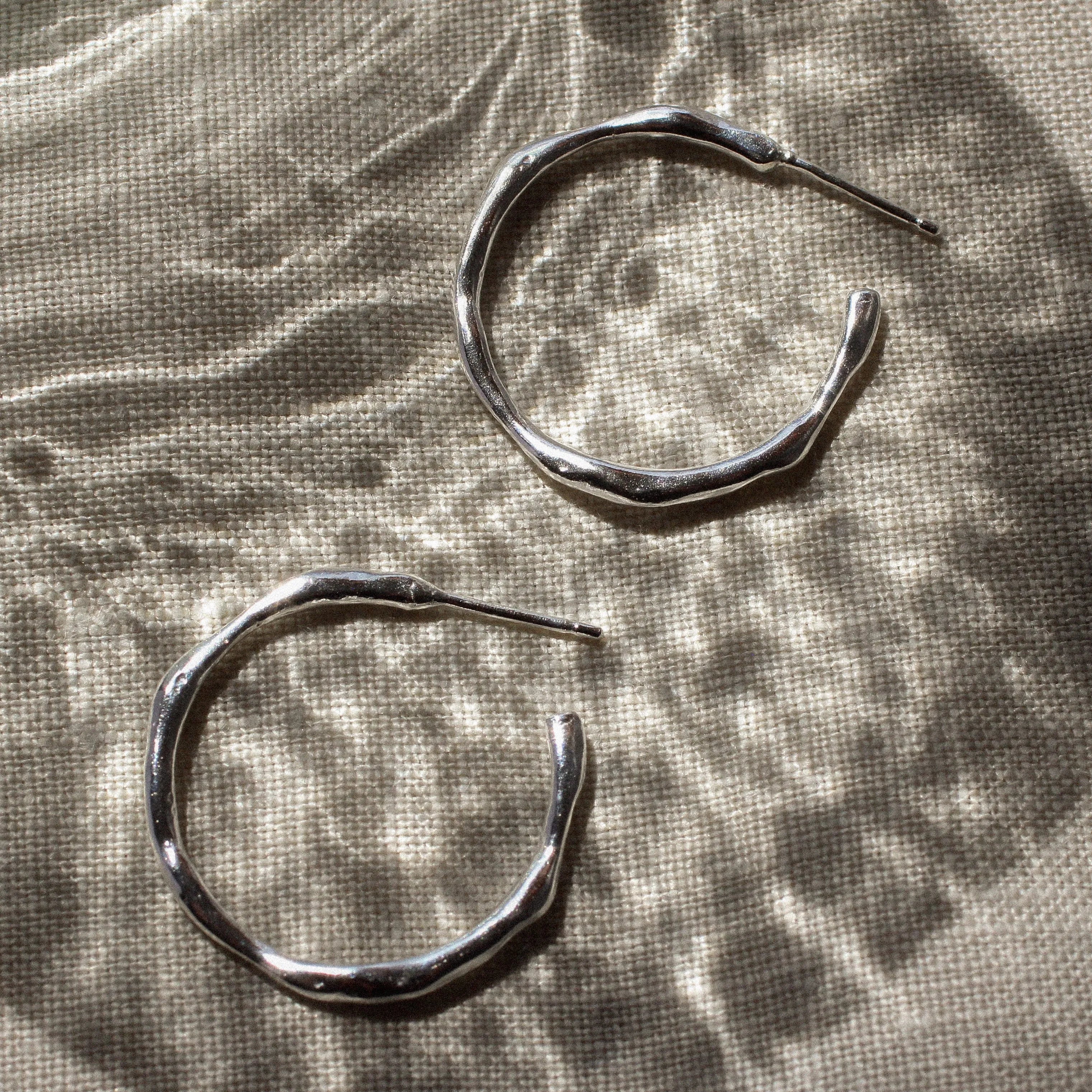 Pair of silver hoop earrings on a textured fabric surface