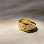 Gold chunky ring with a textured surface on a beige fabric background