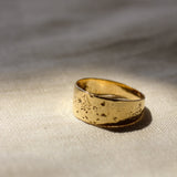 Gold chunky ring with a textured surface on a beige fabric background