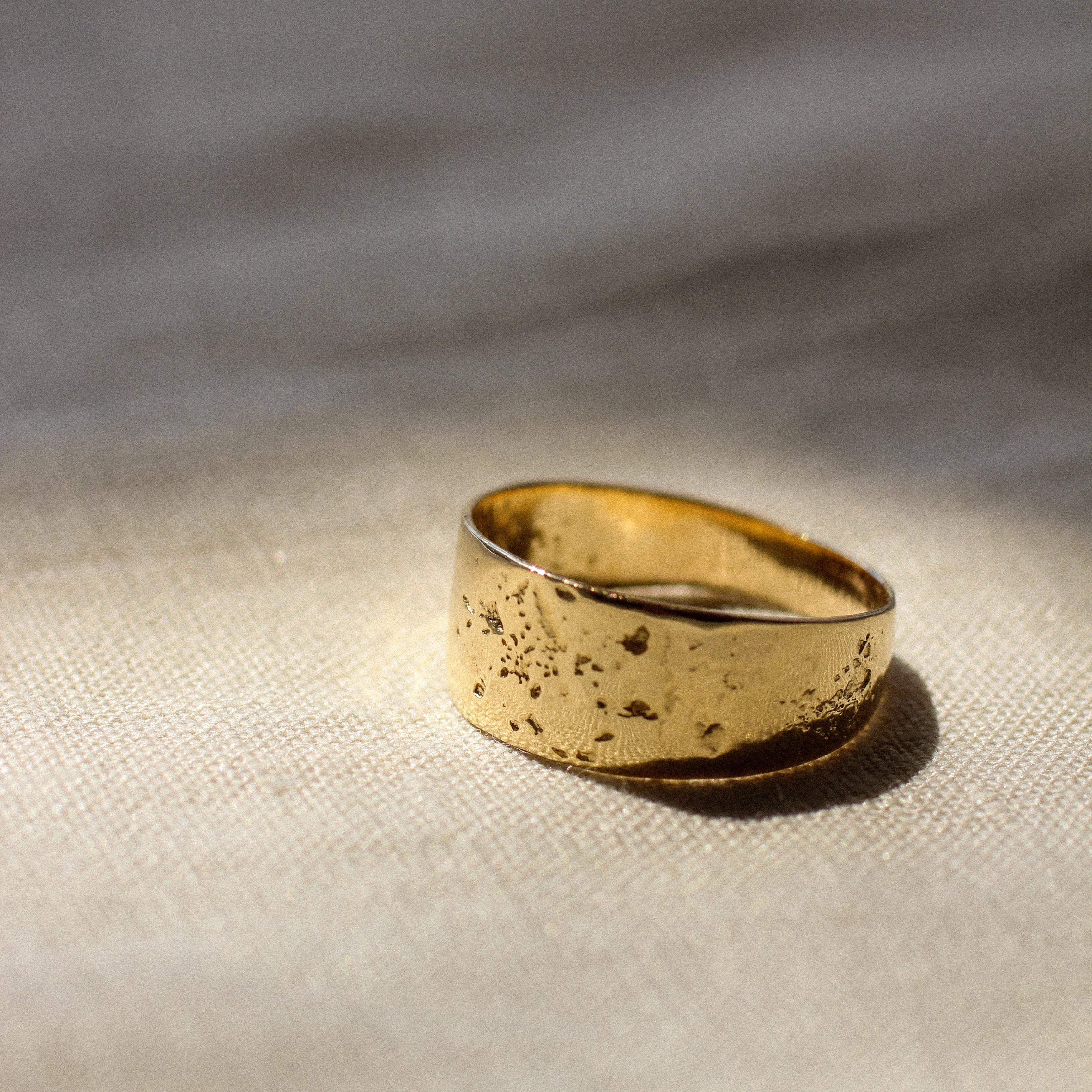 Gold chunky ring with a textured surface on a beige fabric background