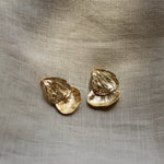 Gold petal earrings on a textured beige fabric background