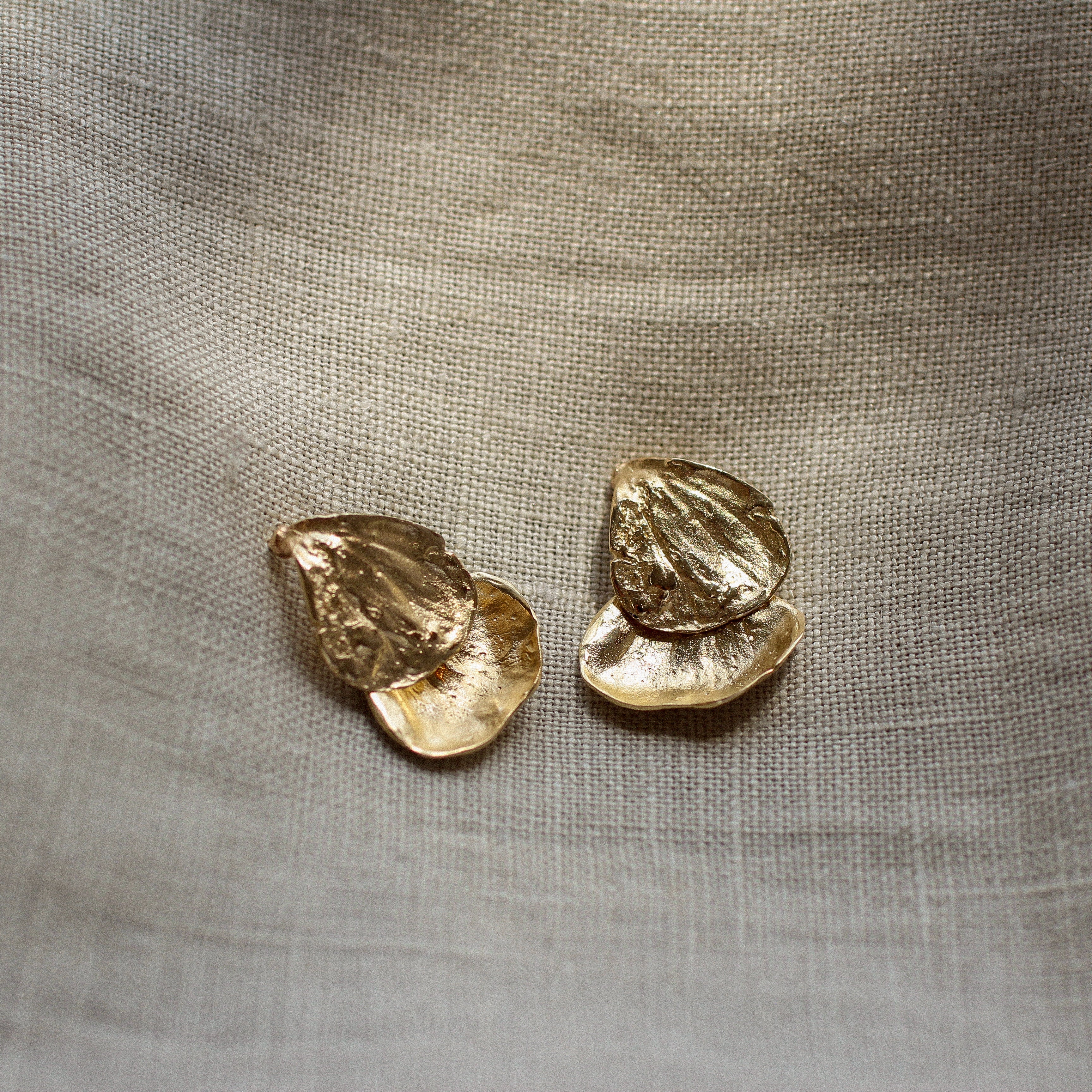 Gold petal earrings on a textured beige fabric background
