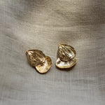 Gold petal earrings on a textured beige fabric background