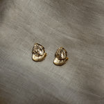 Pair of gold petal shaped earrings on a textured beige fabric background