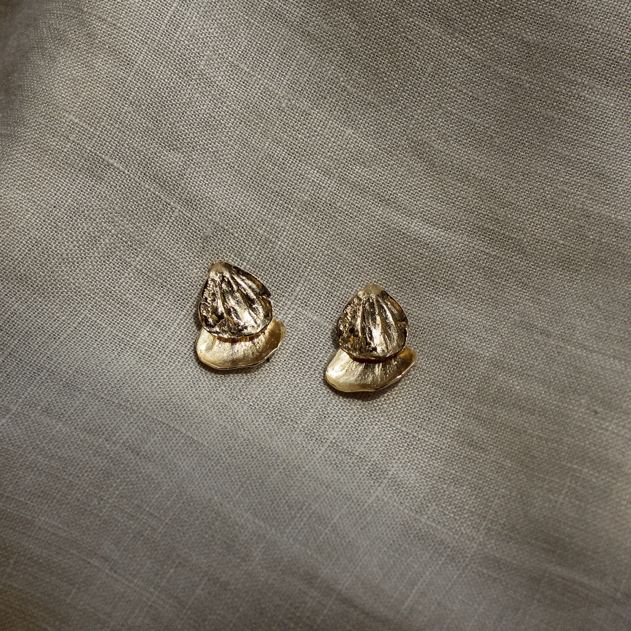 Pair of gold petal shaped earrings on a textured beige fabric background