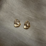 Pair of gold petal shaped earrings on a textured beige fabric background