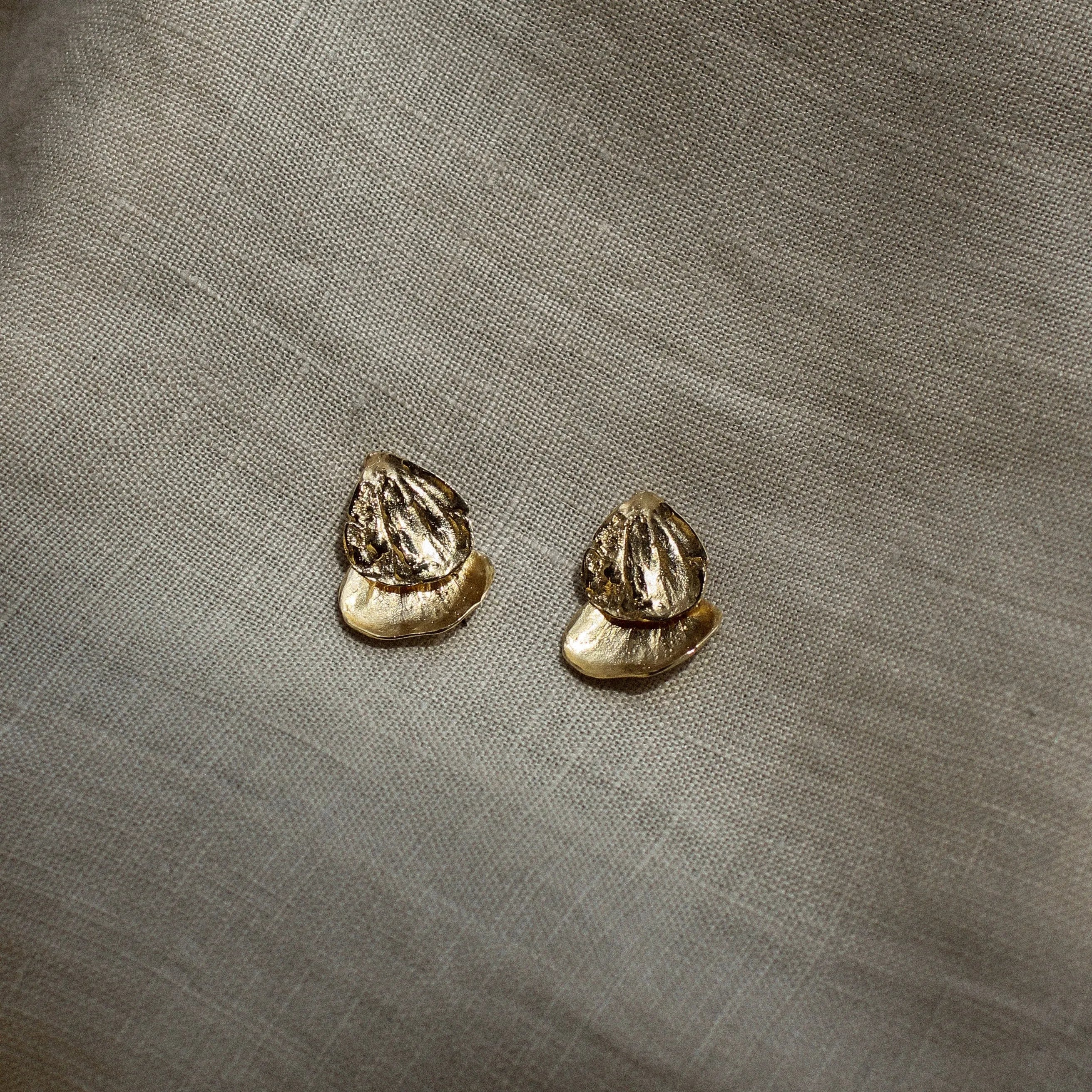 Pair of gold petal shaped earrings on a textured beige fabric background