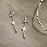 Silver star-shaped earrings and silver bangle on a beige fabric background