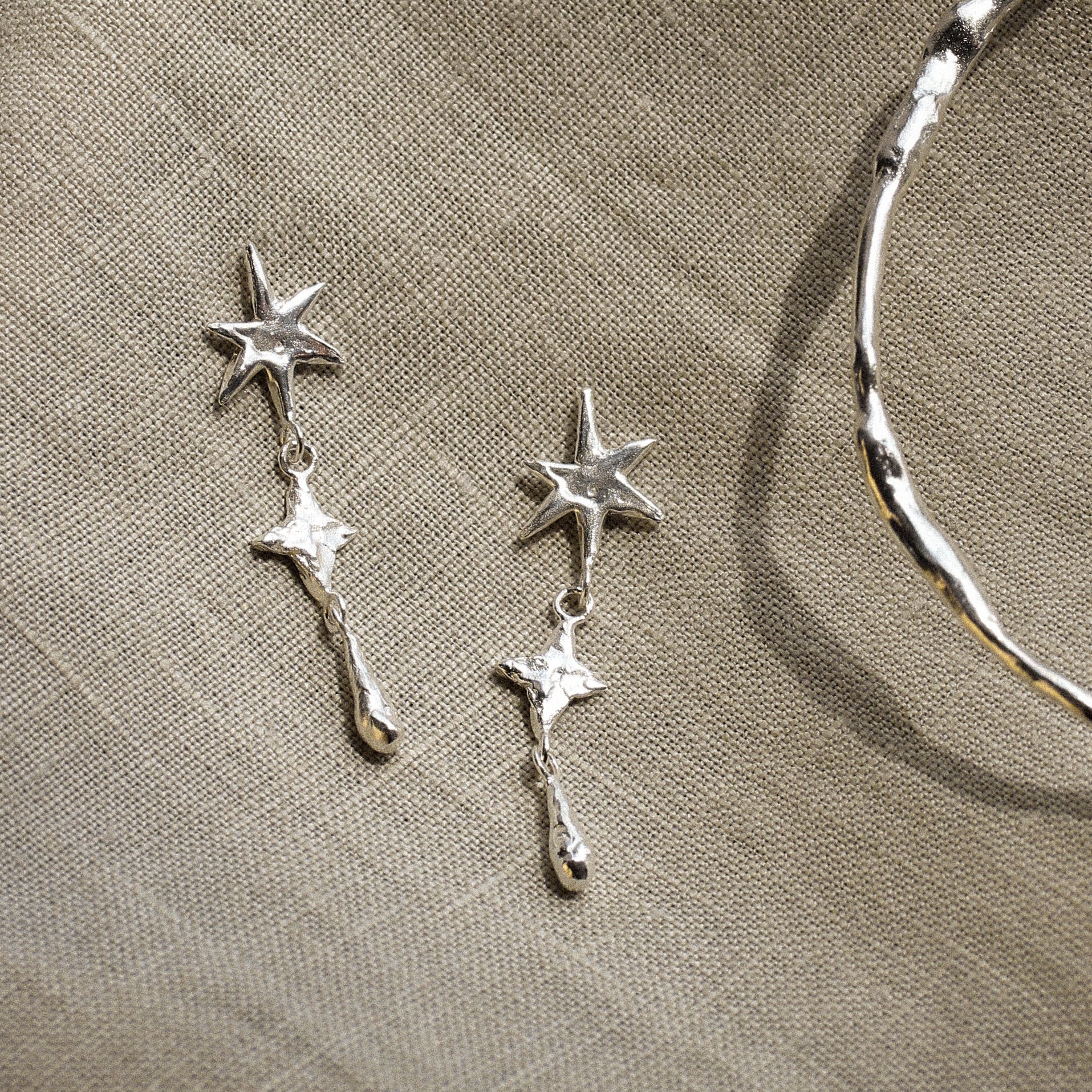 Silver star-shaped earrings and silver bangle on a beige fabric background